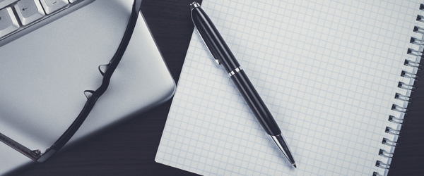 Photo of blank notebook and pen, glasses and laptop